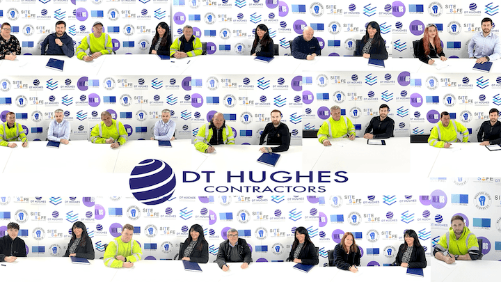 DT Hughes employees signing contracts with an advertising board behind it.